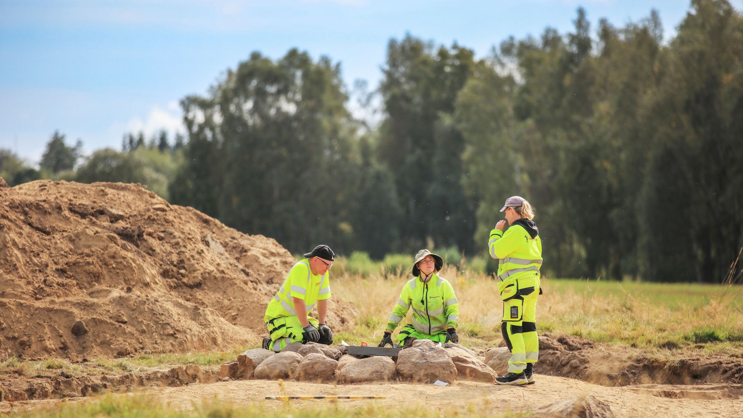 Tre arkeologer arbetar kring en stensättning